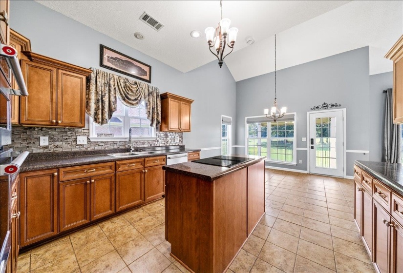 Kitchen featuring a chandelier, dark countertops, tasteful backsplash, a kitchen island, and wood finish cabinets