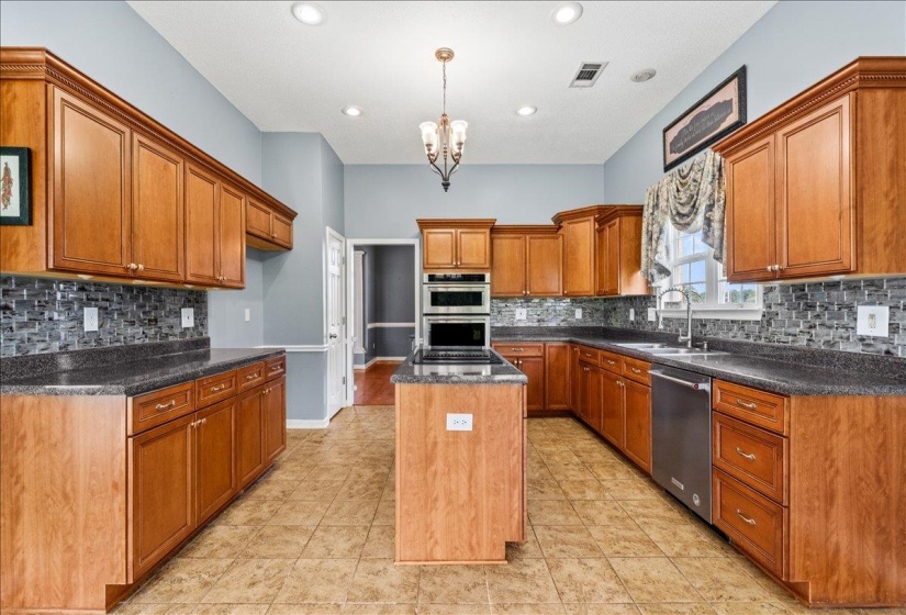 Kitchen with wood finish cabinets, a center island, stainless steel appliances, suspended lighting, and dark stone counters