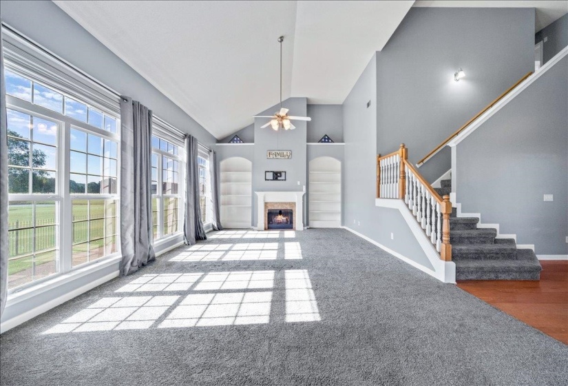 Unfurnished living room with ceiling fan, a glass covered fireplace, built in features, lofted ceiling, and carpet floors