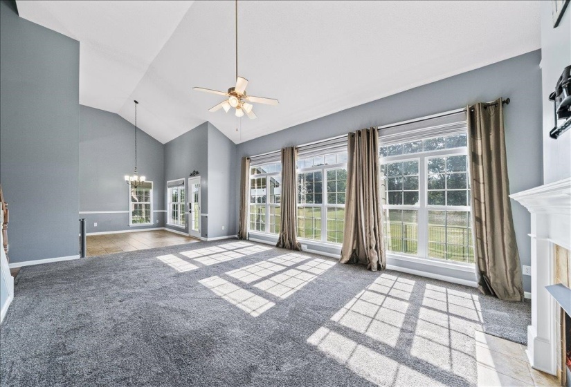 Unfurnished living room featuring a chandelier, ceiling fan, vaulted ceiling, and light carpet