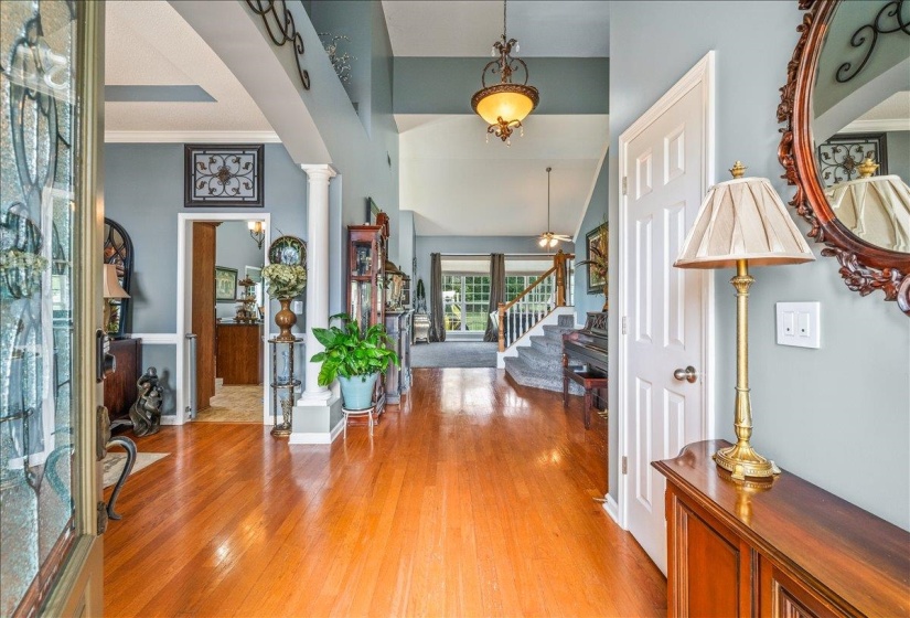 Hardwood flooring extending through the foyer, column architectural accents, vaulted ceilings, decorative overhead lighting fixtures, and a staircase with white balusters