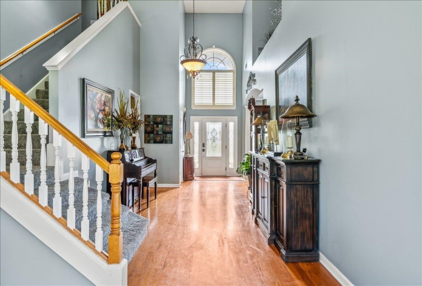 Two-story foyer featuring wood-finish flooring, a grand staircase with carpeted treads and white risers, a wood handrail, and a chandelier