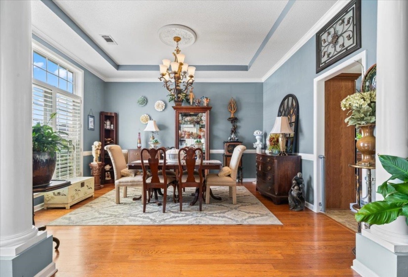Bright dining space featuring hardwood flooring, a tray ceiling with a decorative medallion, white crown molding, and large window with plantation shutters