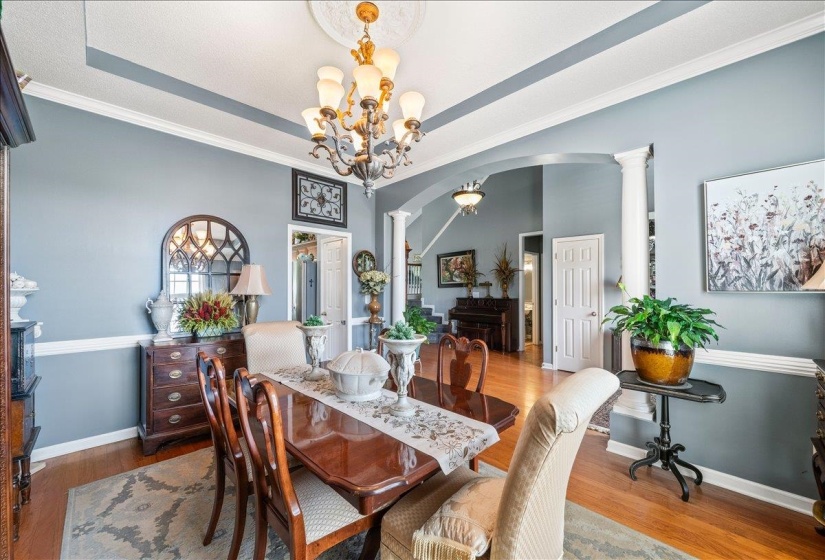 Formal dining area featuring hardwood flooring, crown molding, a tray ceiling with a central chandelier, and a decorative wall mirror