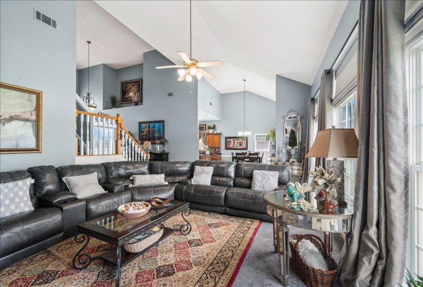 Spacious living area featuring vaulted ceilings, a ceiling fan, and large windows with privacy blinds