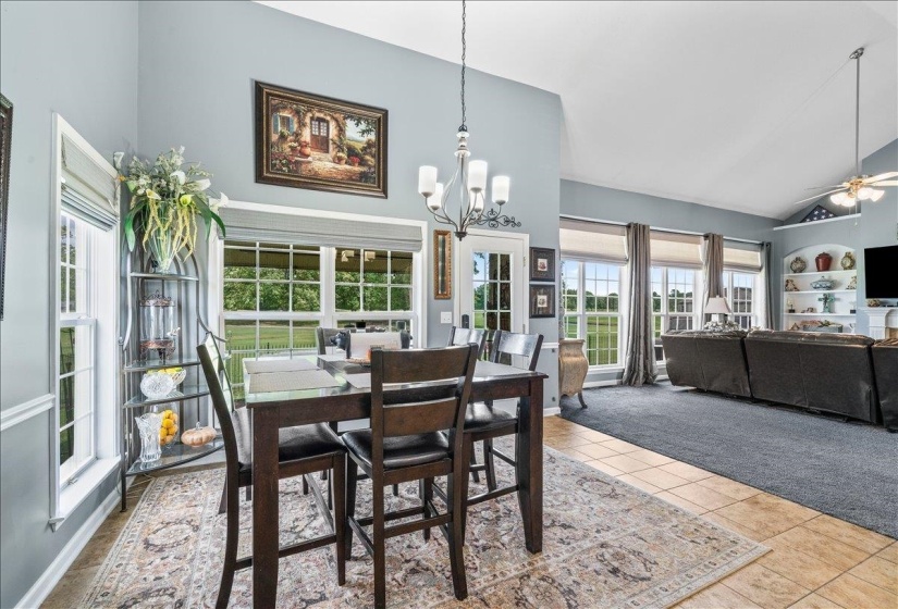 Open-concept living area featuring vaulted ceilings, abundant natural light from multiple windows, and a combination of tile and carpet flooring