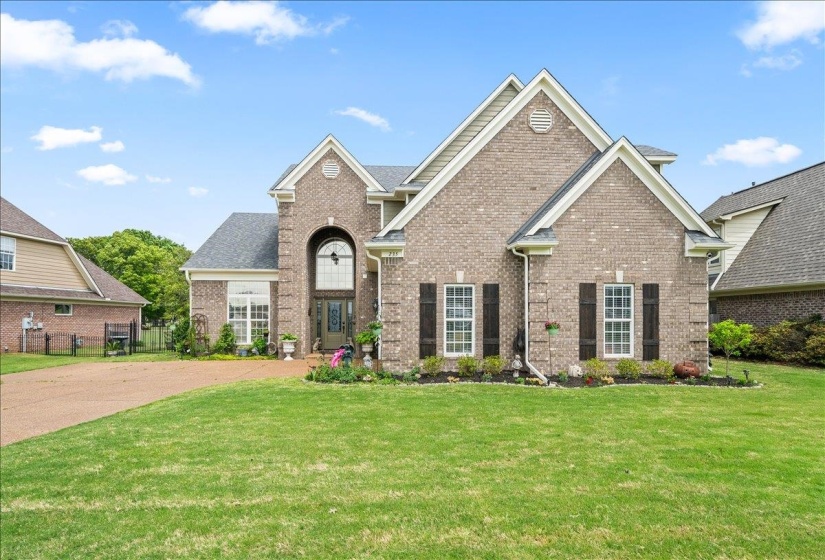 Brick exterior with a prominent arched entry, gabled rooflines, dark shutters, and a well-maintained front lawn