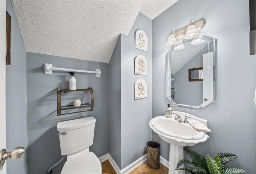 Powder room featuring a white pedestal sink, octagonal mirrored vanity, and a three-light vanity fixture