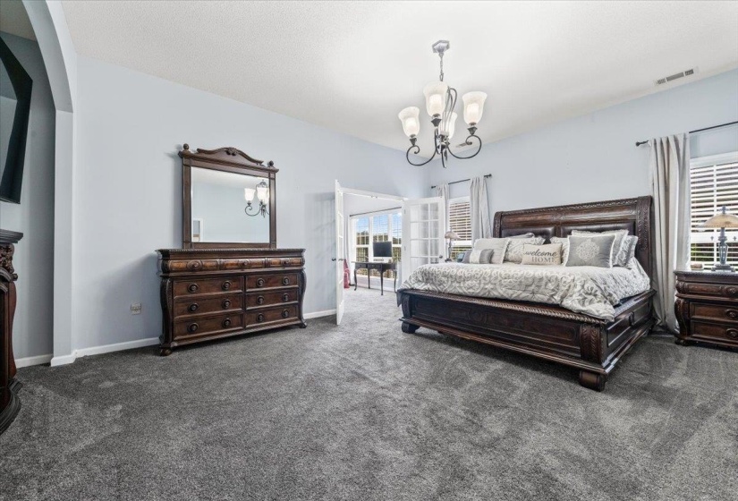 Spacious room featuring light blue walls, gray carpet flooring, and a chandelier lighting fixture