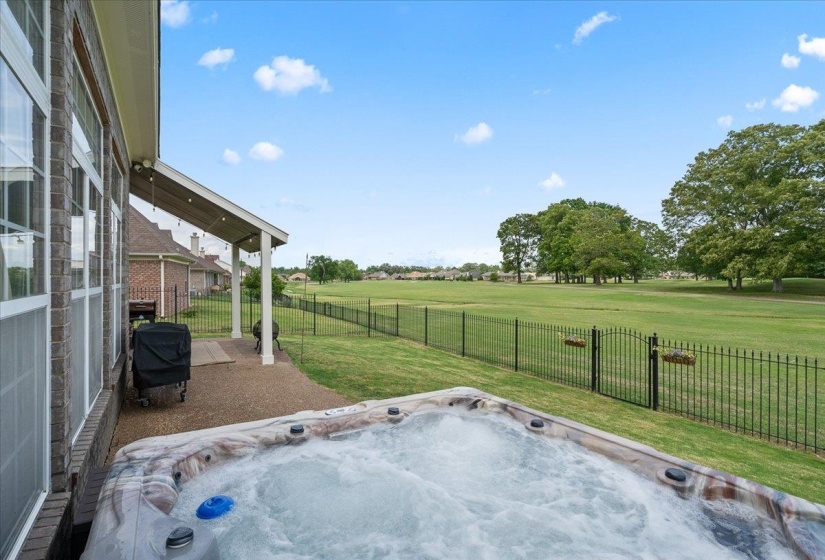 Fenced backyard with a hot tub, a patio, grilling area, and golf course view