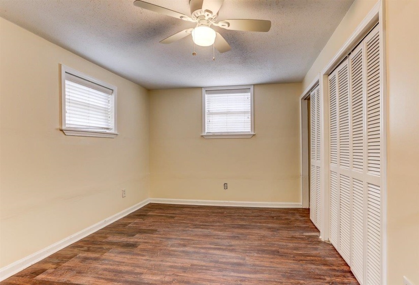 Unfurnished bedroom with multiple closets, a textured ceiling, dark wood finished floors, multiple windows, and a ceiling fan