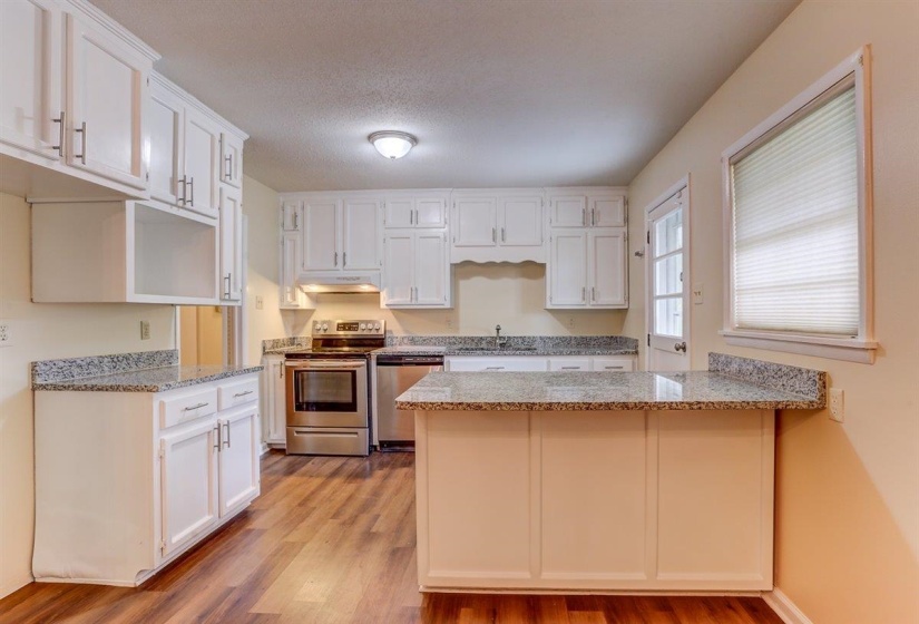 Kitchen featuring stainless steel appliances, a peninsula, light stone counters, light wood finished floors, and white cabinets