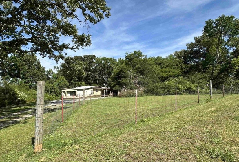 Expansive green lawn with a wire fence and wooded perimeter