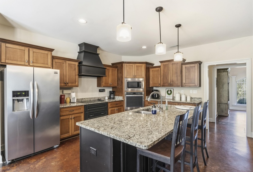 Kitchen featuring stainless steel appliances, wood finish cabinetry, light stone counters, and finished concrete flooring
