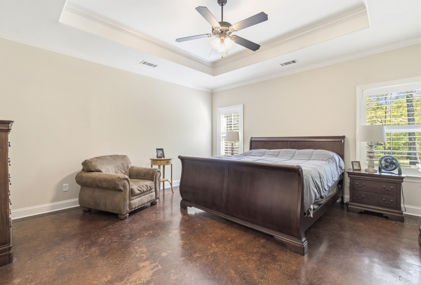 Bedroom with finished concrete floors, ceiling fan, a tray ceiling, and ornamental molding