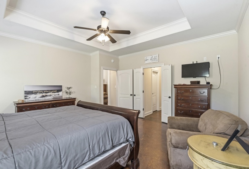 Bedroom with a tray ceiling, ceiling fan, crown molding, and finished concrete flooring