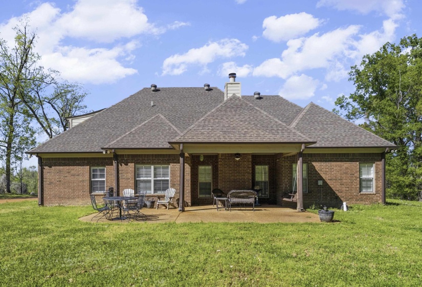 Rear view of house with a patio area, a shingled roof, brick siding, a chimney, and a lawn