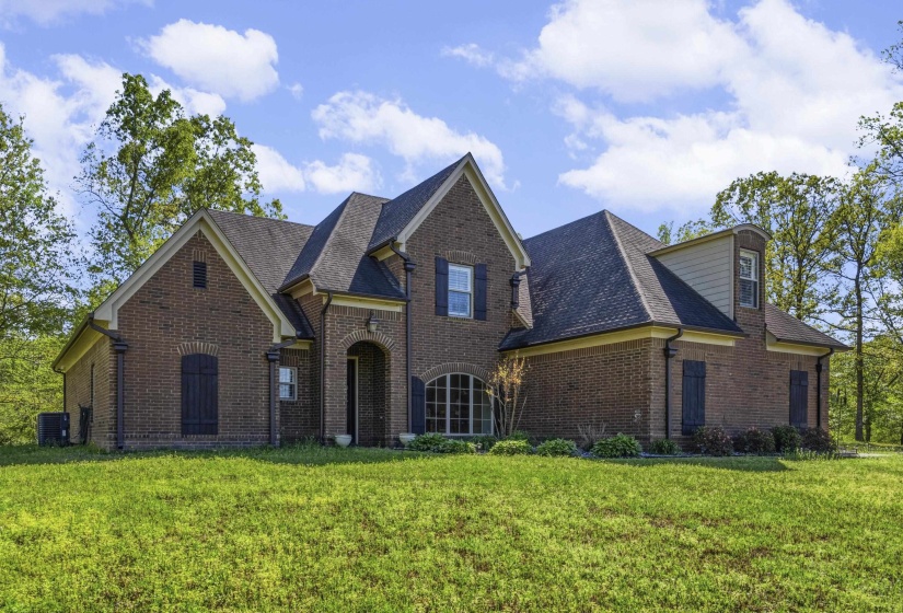 French country inspired facade with brick siding, roof with shingles, and a front lawn