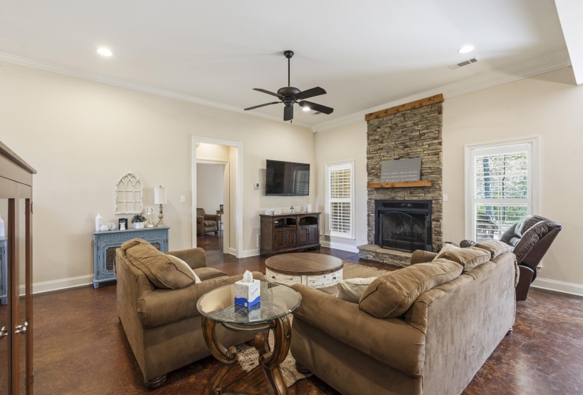 Living area with a stone fireplace, concrete flooring, plenty of natural light, crown molding, and recessed lighting
