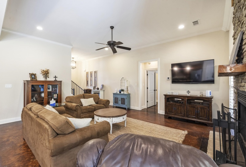 Living room featuring a stone fireplace, ornamental molding, and ceiling fan