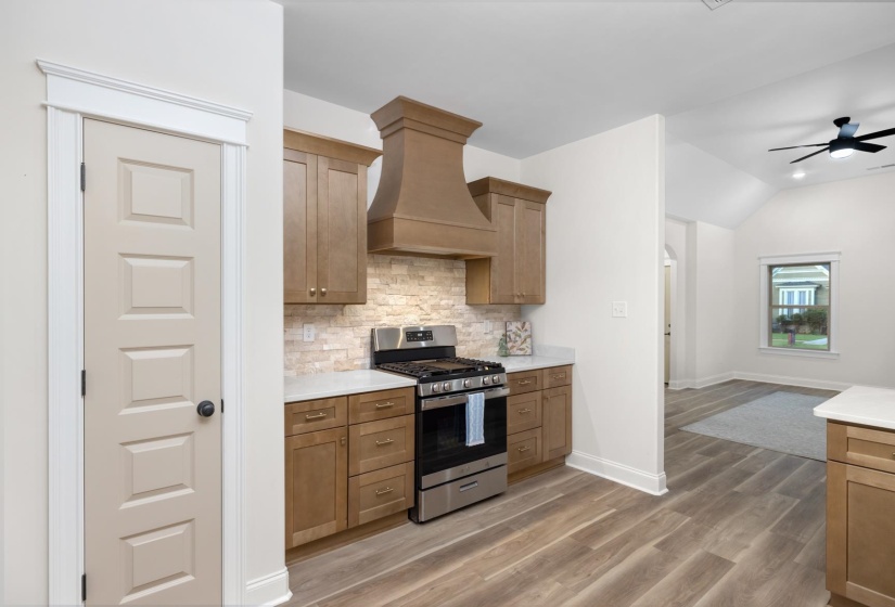 Kitchen featuring wood-finish cabinetry, stainless steel range with matching hood, light-toned stone backsplash, and light countertops