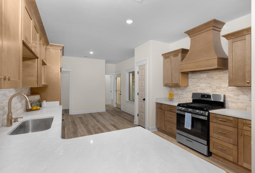 Kitchen featuring light wood-tone cabinetry, stainless steel appliances, stone-look backsplash, white countertops, and wood-finish flooring