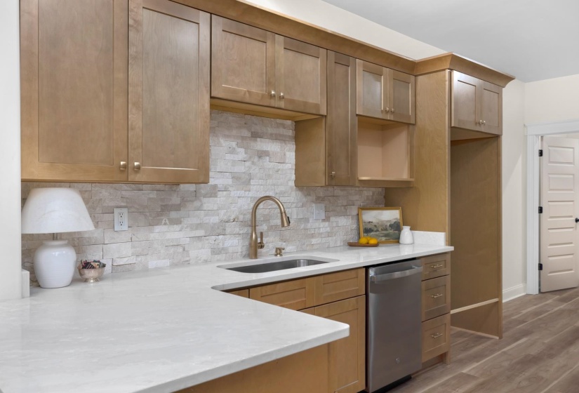 Kitchen showcasing light wood cabinetry with gold-tone hardware, a stacked stone backsplash, and a white countertop