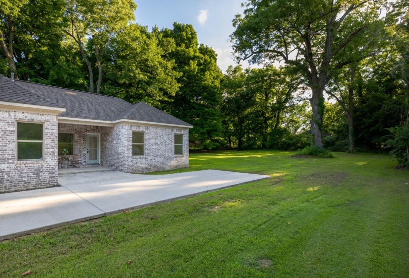 Spacious green lawn featuring mature trees and a concrete patio