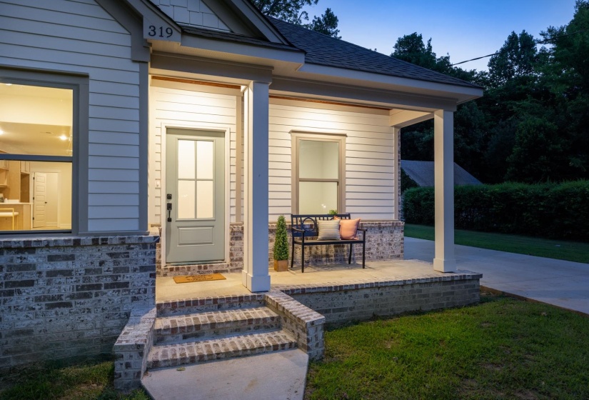 Charming facade featuring white siding, a contrasting brick foundation, and a covered front porch with recessed lighting