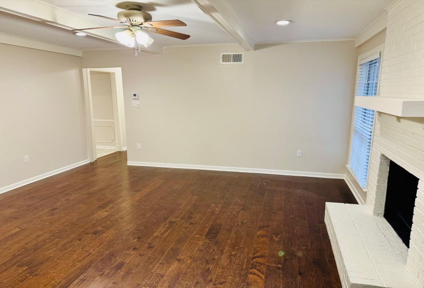 Unfurnished living room with crown molding, a brick fireplace, dark hardwood / wood-style flooring, ceiling fan, and beam ceiling