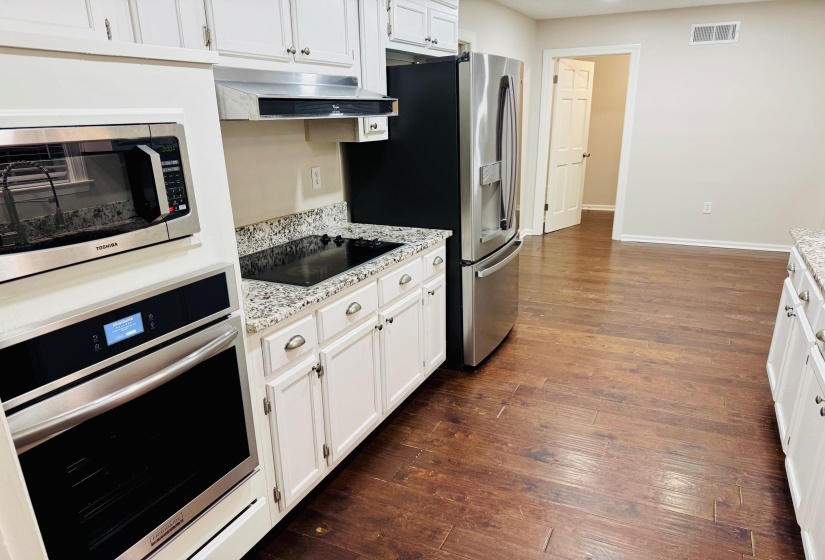 Kitchen featuring dark wood-type flooring, stainless steel appliances, light stone countertops, white cabinets, and wall chimney exhaust hood