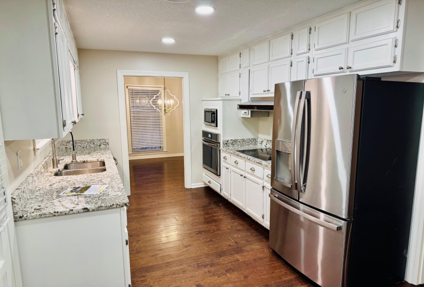 Kitchen with dark hardwood / wood-style floors, white cabinetry, sink, stainless steel appliances, and light stone countertops