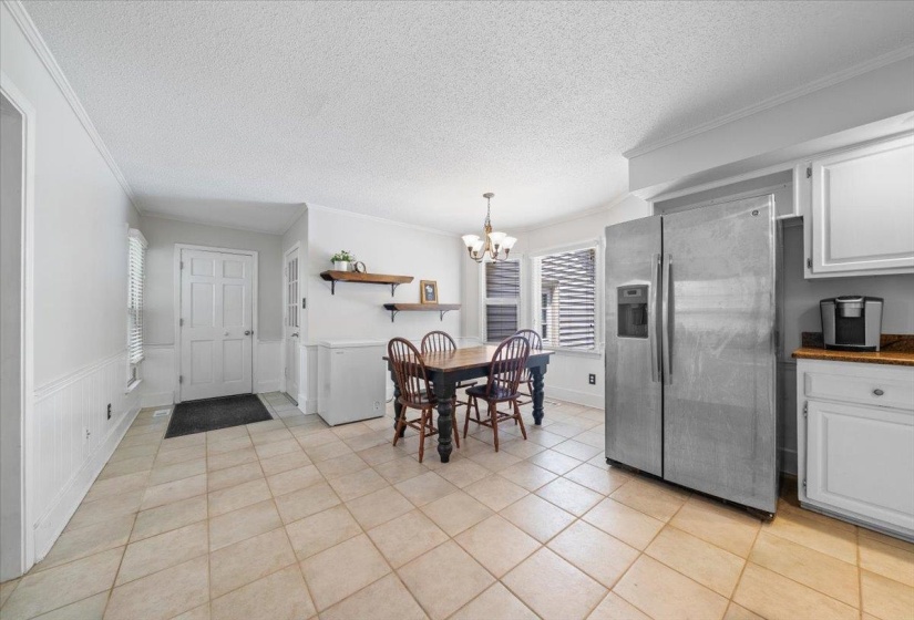 Dining room featuring a chandelier, a textured ceiling, ornamental molding, light tile patterned flooring, and a wainscoted wall