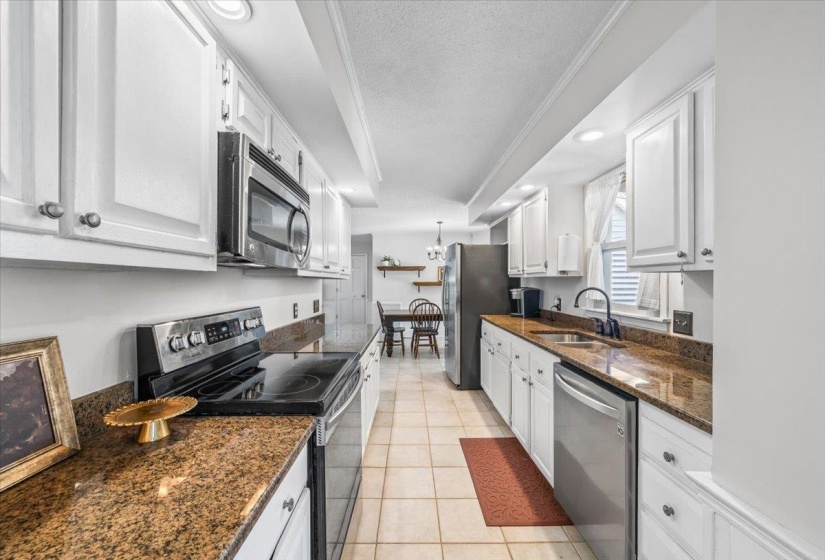 Kitchen with appliances with stainless steel finishes, a textured ceiling, white cabinetry, light tile patterned flooring, and dark stone countertops