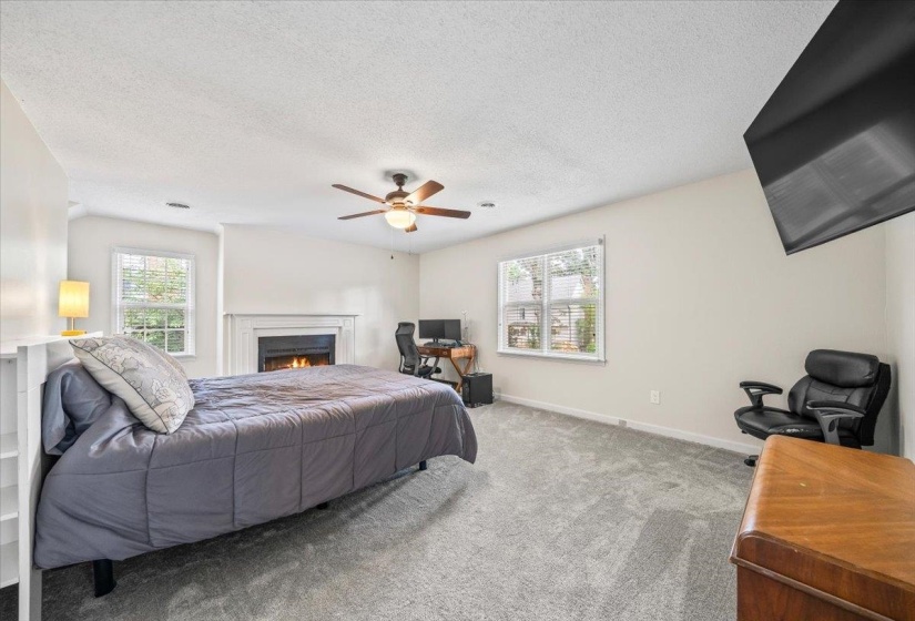 Bedroom featuring a warm lit fireplace, a textured ceiling, carpet flooring, and a ceiling fan