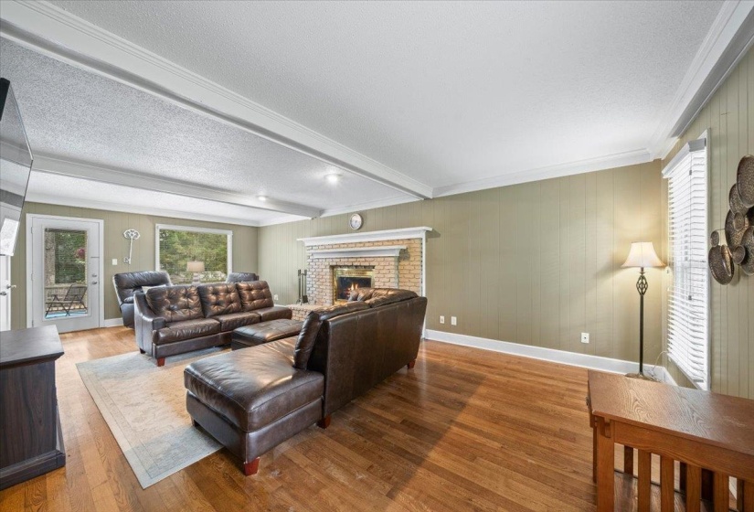 Living area featuring a textured ceiling, wood finished floors, a brick fireplace, beamed ceiling, and ornamental molding