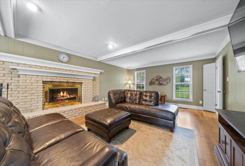 Living area with wood finished floors, a textured ceiling, beam ceiling, a brick fireplace, and ornamental molding