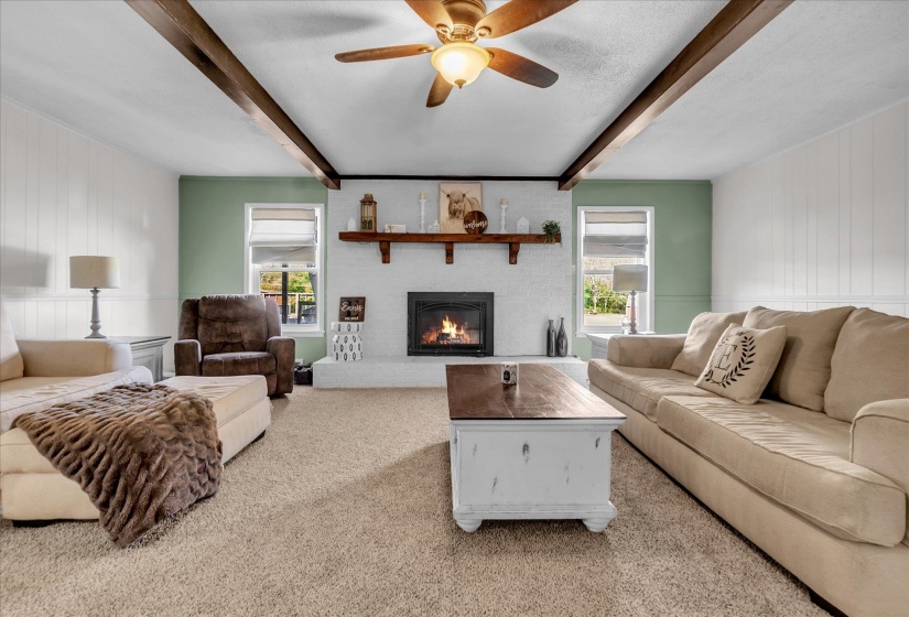 Carpeted living area featuring beam ceiling, a fireplace, wood walls, a ceiling fan, and a decorative wall