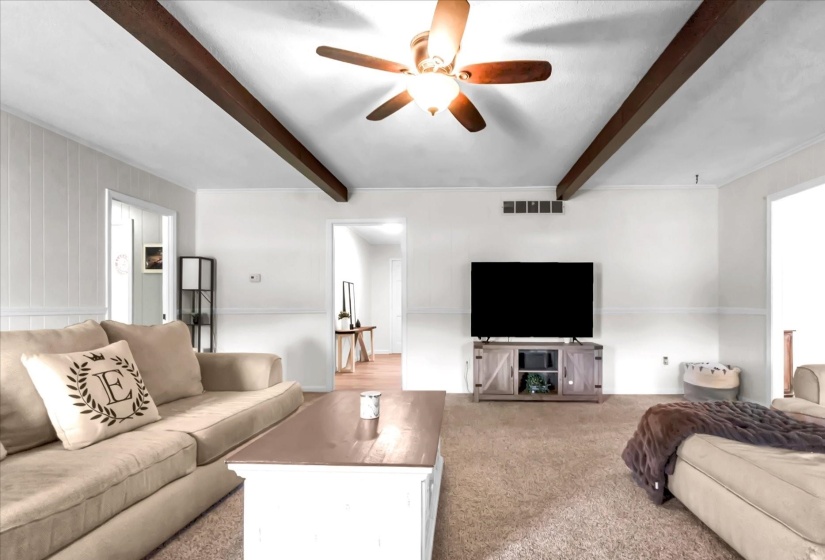 Carpeted living room with beam ceiling and ceiling fan