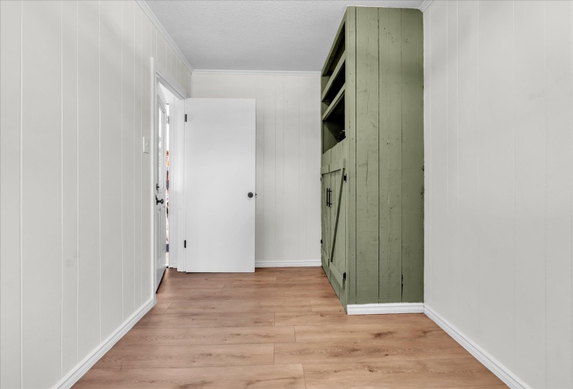 Corridor with light wood-type flooring, wooden walls, crown molding, and a textured ceiling