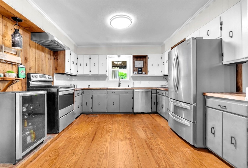 Two tone kitchen featuring ornamental molding, two tone cabinetry, stainless steel appliances, light wood-style flooring, and exhaust hood