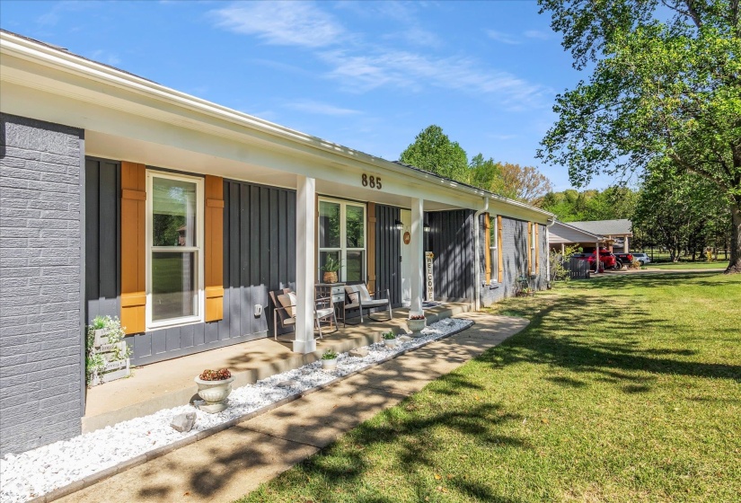 Rear view of property featuring a porch, a lawn, board and batten siding, and brick siding