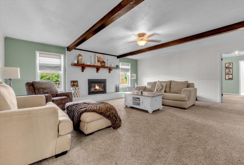 Carpeted living area with ceiling fan, a brick fireplace, beam ceiling, and a textured ceiling