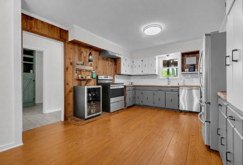 Kitchen featuring two tone cabinetry, ornamental molding, stainless steel appliances, wooden walls, and light wood-type flooring