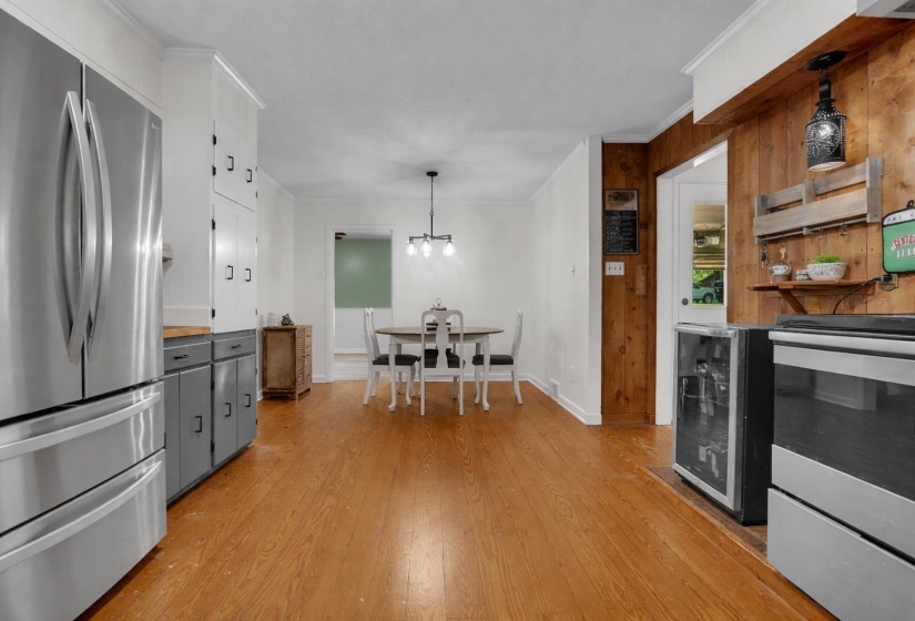 Two tone kitchen featuring stainless steel appliances, dual tone cabinetry, crown molding, wine cooler, and pendant lighting