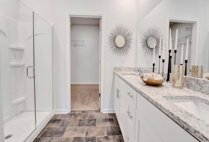 Full bath featuring a walk in closet, double vanity, a shower stall, and stone finish floors