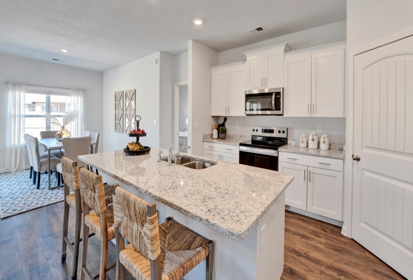 Kitchen with a kitchen bar, stainless steel appliances, white cabinets, light stone countertops, and dark wood-style flooring