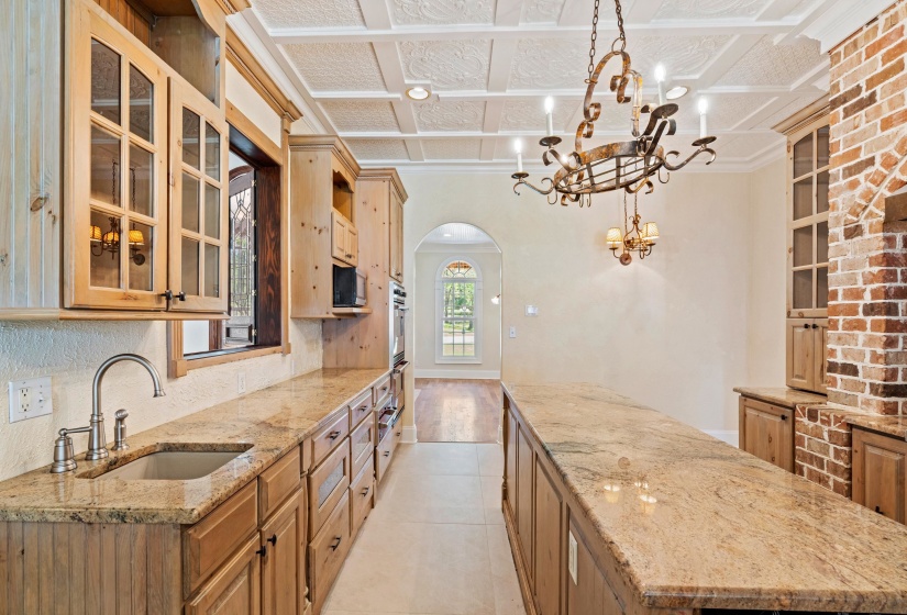 Kitchen featuring glass fronted cabinets, arched walkways, a center island, light stone counters, and crown molding