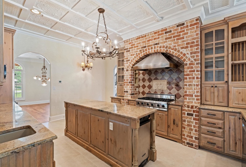Kitchen with a kitchen island, light stone counters, arched walkways, a chandelier, and ornamental molding