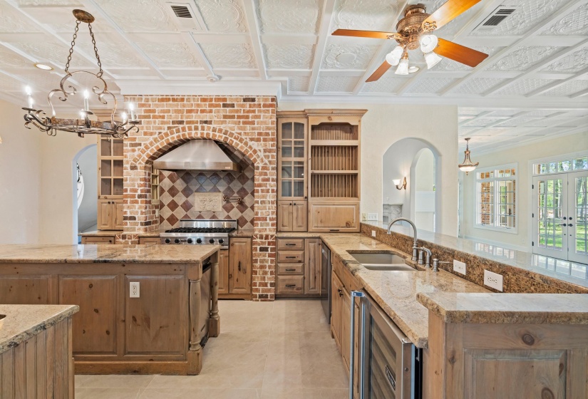Kitchen with light stone countertops, wine cooler, crown molding, glass insert cabinets, and decorative backsplash